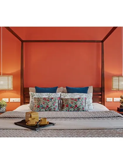 A close-up of the master bedroom in Nataraj House, where the terracotta wall, tropical-print cushions, and cane lights come together to create a serene escape.