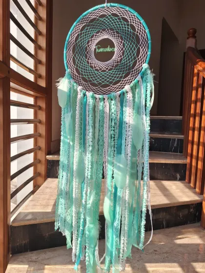The teal green dreamcatcher catching the sunlight, highlighting the intricate web and the delicate feathers. A perfect piece for bringing positive vibes indoors.