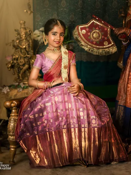 A young girl dressed in a traditional silk lehenga for a 'Moggina Jade' ceremony. The photo captures the elegance and cultural significance of the event.