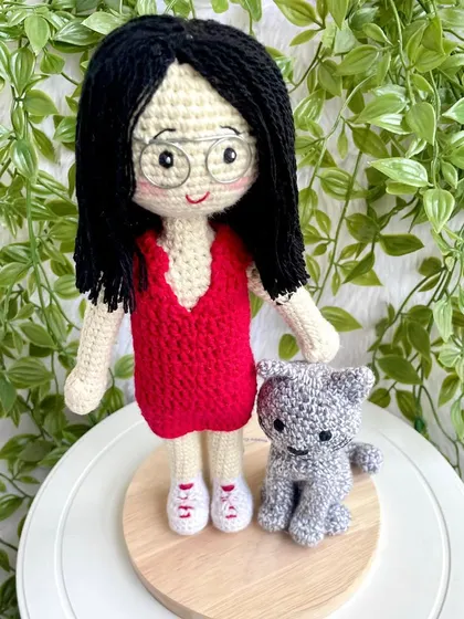 A thoughtful farewell gift for a niece heading off to higher studies. This replica doll in a red dress stands with her pet cat on a display base, a reminder of home she can take with her.