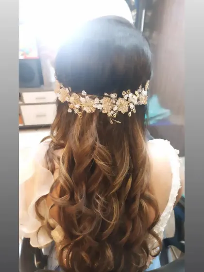 A half-up hairstyle with soft curls, adorned with a beautiful golden floral hair accessory. This is a perfect look for an engagement or Roka ceremony.