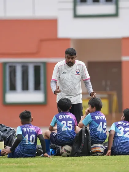 A coach gives a tactical talk to a group of players sitting on the grass. These strategy sessions are crucial for learning and improvement during tournaments.