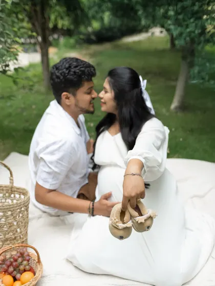 A classic and heartwarming pose for any pregnancy photoshoot. The couple holds up a tiny pair of baby shoes, symbolizing the new life they are about to welcome.