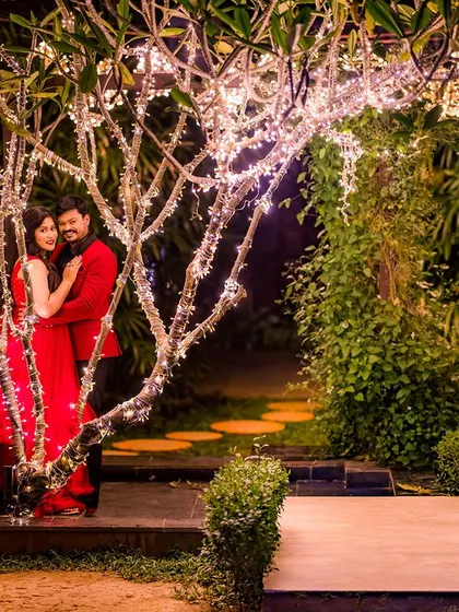 A romantic portrait by a tree adorned with fairy lights. The couple's red outfits pop against the dark background, creating a passionate and festive feel.