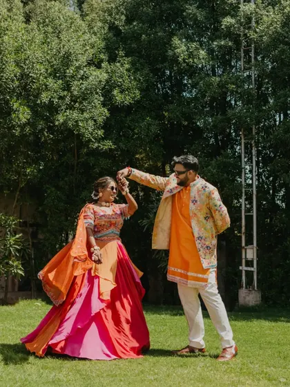 A romantic moment as the groom twirls his bride in a lush green setting. This playful and happy shot is a highlight of their Haldi carnival celebration.