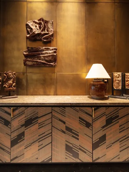 The entrance foyer features a console with marquetry shutters and an installation by Revati Sharma Singh. The walls are paneled in antique brass, setting a tone of rich materiality and craftsmanship from the moment one enters.