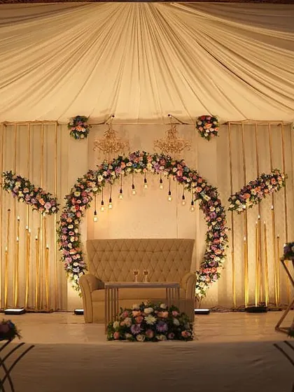 An elegant engagement stage with a circular floral arch and hanging Edison bulbs. The neutral-toned sofa and soft lighting create a warm and romantic ambiance.