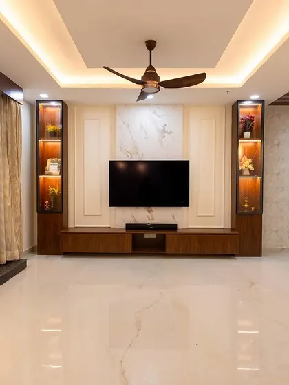 This living room design focuses on creating a grand entertainment center. The TV is flanked by two illuminated display cabinets, all set against a marble-paneled wall, creating a dramatic and elegant focal point.