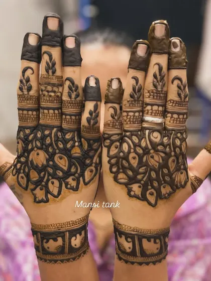 This design features bold, dark-filled floral patterns on the palms, contrasted with delicate leafy designs on the fingers. This style creates a striking and modern look for any bride.