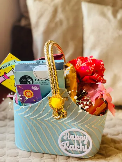 A similar blue fabric basket from another angle, showing a "Happy Rakhi" card and other treats for the occasion.