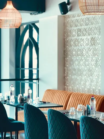 The thoughtful details of our dining area, from the quilted teal chairs and warm wood tables to the patterned wall textures and ambient lighting.