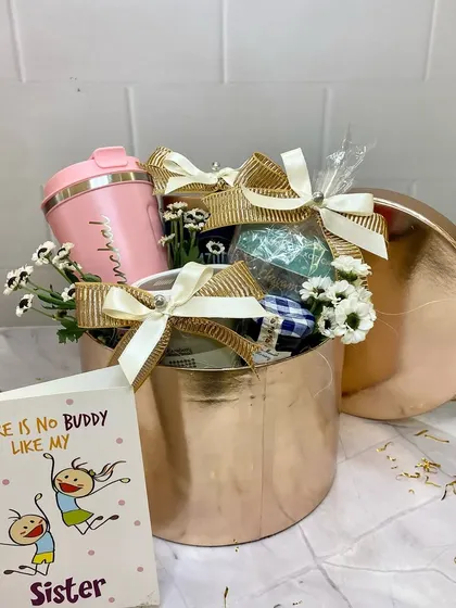 There's no buddy like my sister. This rose gold hamper is curated for a sister, featuring a personalized tumbler and other pampering gifts, all tied together with beautiful bows and flowers.