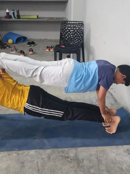A creative double plank variation where the base partner's feet are against the wall, changing the dynamic of the pose.
