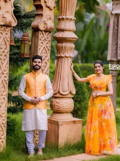 A stylish portrait of a couple in coordinated yellow and white outfits, standing by ornate pillars. This shot is both modern and traditional.