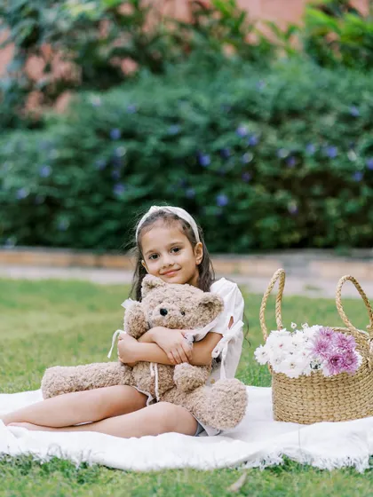 A little girl holding her teddy bear during an outdoor picnic session. The simple props add a touch of sweetness to the photos.