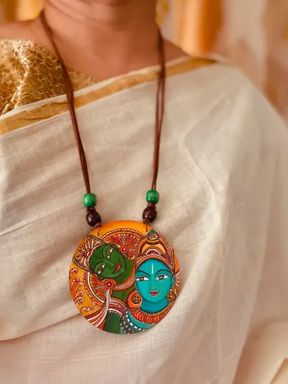The Kerala mural pendant worn against a classic off-white and gold saree, a perfect pairing that exudes subtle elegance.