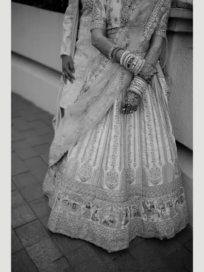 A black and white detail shot of the bride's intricately embroidered lehenga, focusing on the texture and craftsmanship.