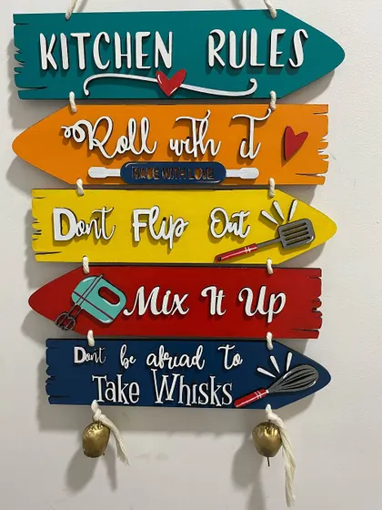 A full view of the hanging kitchen sign. It's made from separate wooden planks, each painted with a different color and fun quote.