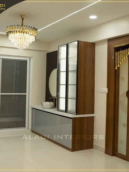 A sophisticated dining area featuring a stunning crystal chandelier and a custom crockery unit with a built-in wash basin. The frosted glass doors of the puja room add another layer of design.