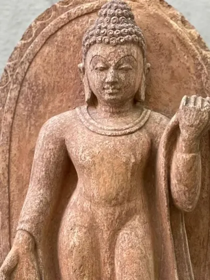 A standing Buddha statue carved in the Pala dynasty style from red sandstone. The details of the robe and the calm posture create a feeling of peace, making it a beautiful statement piece for a garden or indoor space.