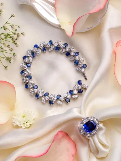 A breathtaking sapphire and diamond bracelet and ring set. Styled with delicate rose petals on a soft satin cloth, this shot evokes a sense of romance and timeless luxury.