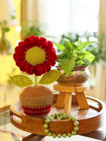 The red potted flower paired with a real plant, showing how handmade and natural elements can complement each other beautifully.