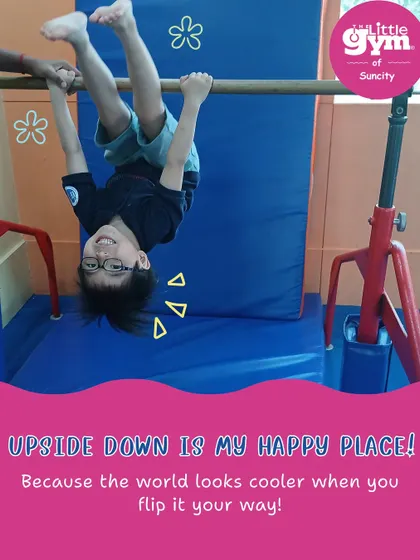 Upside down is a happy place! A child joyfully hangs from the gymnastics bar, building upper body strength while smiling from ear to ear.