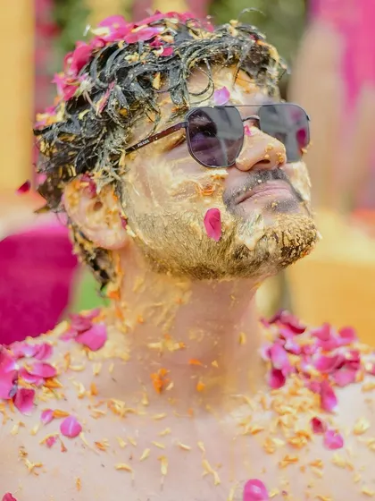 A close-up shot of the groom covered in haldi and petals, looking up with a cool expression. This portrait is both artistic and full of character.