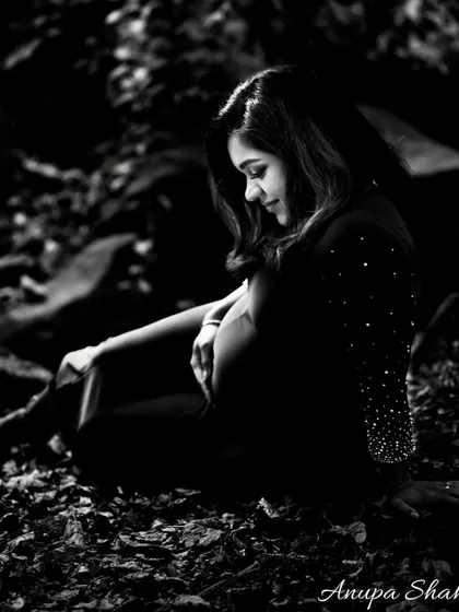 A moody and artistic black and white maternity portrait. The expectant mother is seated in a forest setting, creating a quiet, contemplative, and beautiful image.