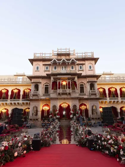 The grand aisle leading to the wedding ceremony at Chomu Palace. A regal red carpet is flanked by lush floral arrangements, setting a majestic tone for the evening.