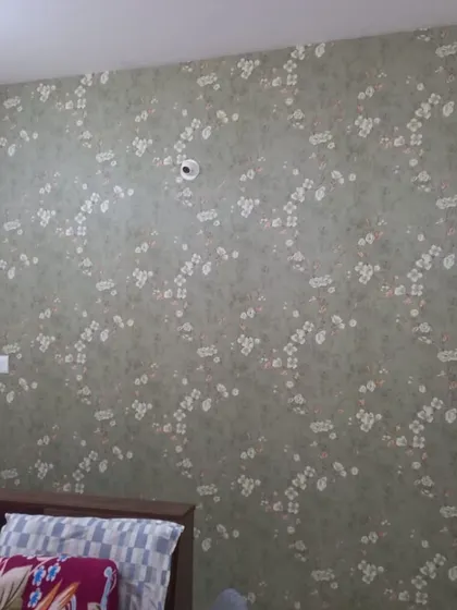 A bedroom wall featuring a subtle green wallpaper with a delicate white floral pattern. The design is soft and restful, perfect for creating a peaceful sleeping environment.