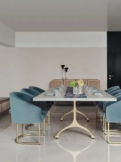 A bright and modern dining area defined by soft blue velvet chairs and a sleek white tabletop. A distinctive blue tiled partition adds a pop of color and texture to the clean, minimalist space.