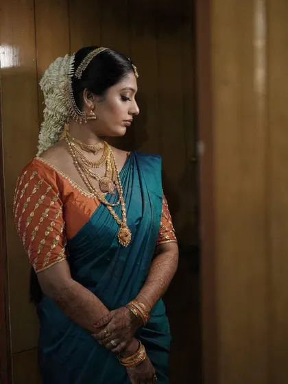A side profile showcasing the elegant hair updo and the smooth finish of the makeup. The hair is adorned with traditional flowers and a hair accessory.