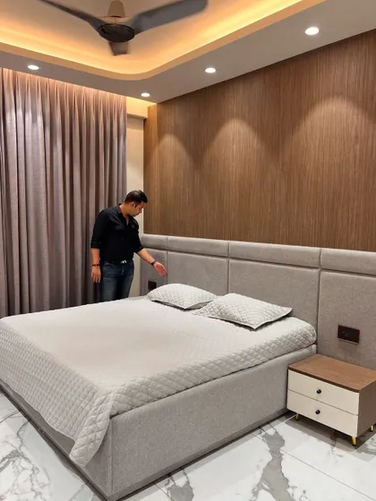 A happy handover of this bedroom. The design features a simple, elegant upholstered headboard against a wood-paneled wall, with warm cove lighting.