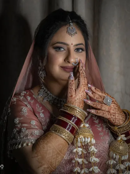 A close-up of the bride in a traditional 'namaste' pose, showcasing her intricate henna, bridal chooda, and kalire.