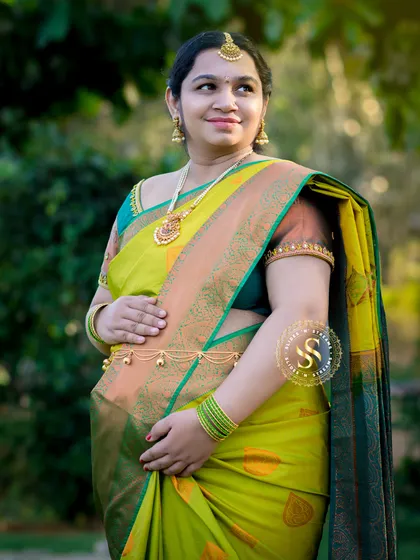 The elegance of a traditional saree is unmatched. This outdoor portrait captures the beauty and grace of a mom-to-be in a vibrant lime green silk saree, complemented by traditional jewelry and soft, natural lighting.