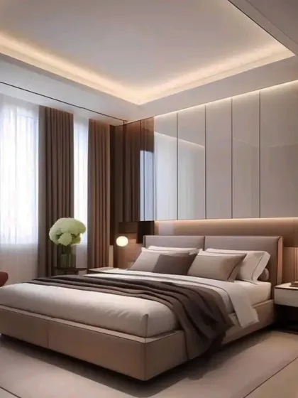 A clean and modern bedroom design with a glossy white paneled wall and a false ceiling with soft, indirect lighting. The large windows with sheer curtains allow for plenty of natural light.