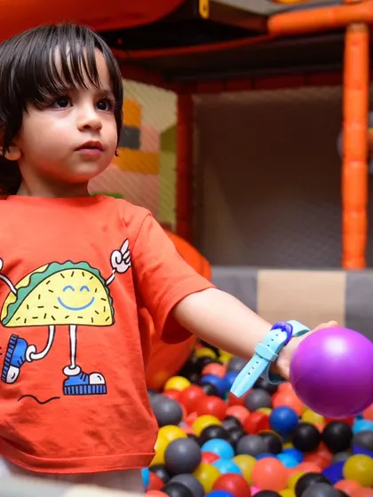 A boy in a taco shirt holds a purple ball, ready to play in the giant ball pit.