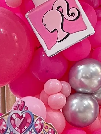 A close-up of a Barbie-themed balloon garland, featuring a nail polish prop and a princess tiara cutout.