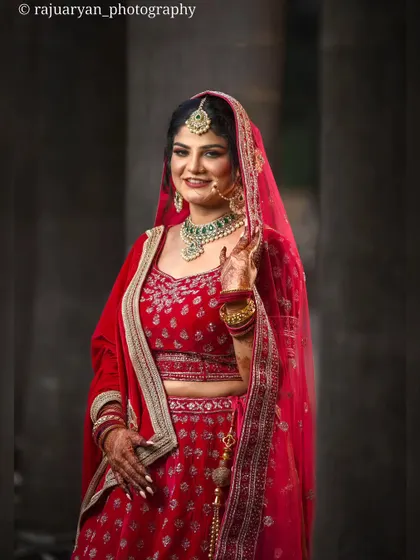 A classic bridal portrait showcasing the elegance of the bride. Her smile and pose radiate happiness and confidence in her beautiful red wedding lehenga.