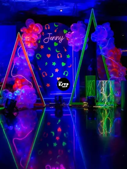 Glow mode: ON. A spectacular neon party setup with a blacklight backdrop, glowing geometric frames, and fluorescent decor that reflects beautifully on the shiny floor.