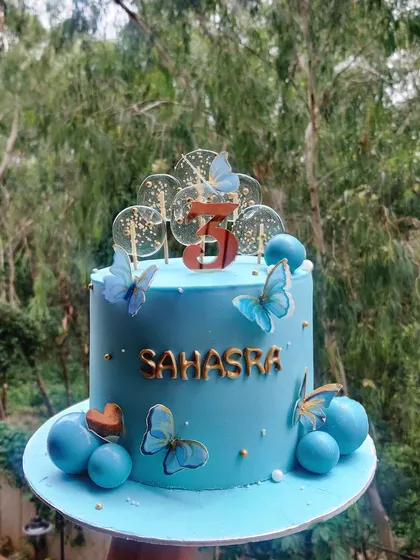 A beautiful blue butterfly cake celebrating a third birthday. The design features delicate butterflies and shimmering lollipops, making it a truly magical and celebratory piece.
