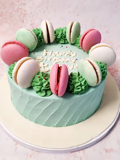 We combine two French classics in this elegant macaron cake. A ring of colorful macarons in pink, white, and mint green sits atop a pastel green cake, creating a simple, chic, and delicious design for a birthday.