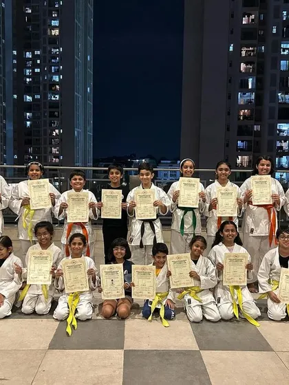 Students from our Prestige Falcon City dojo pose with their new belts and certificates against the Bangalore city skyline, marking a significant milestone in their karate journey.