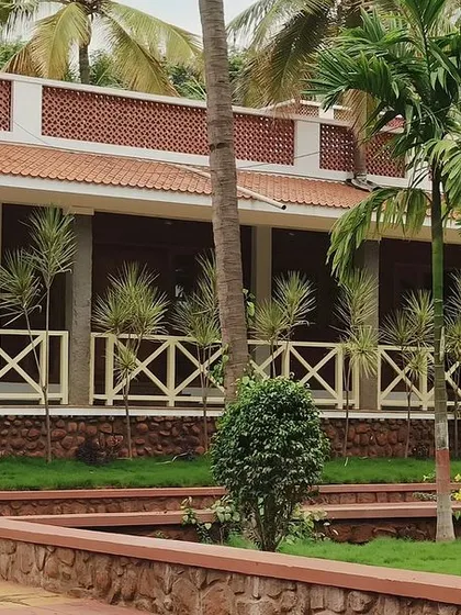 A side view of the farmhouse veranda. The design uses simple, rustic materials like laterite blocks and wooden railings to create an authentic, earthy ambiance.