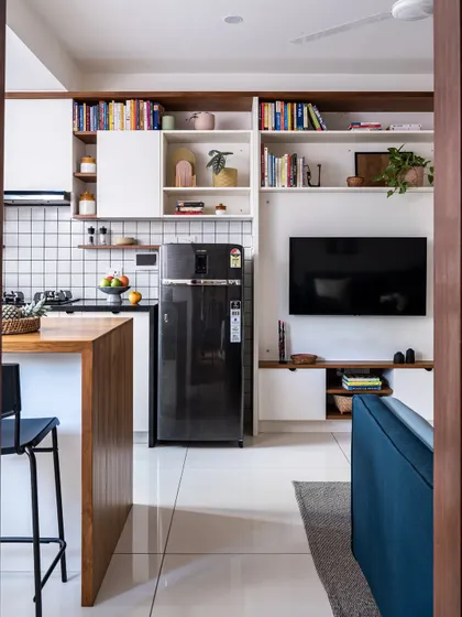 In the 'Footloose' studio apartment, the kitchen, living, and dining areas are one unified space. The design features open shelving for books and decor, seamlessly integrating the kitchen with the living area.