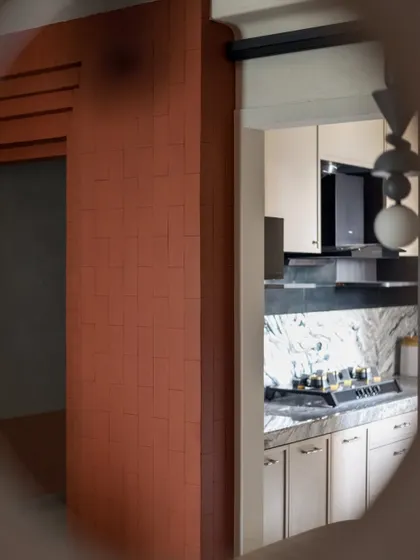 A sneak peek into the kitchen of 'A Den', seen through a circular cutout. The terracotta brick wall and modern kitchen create a beautiful contrast.