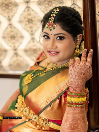A happy bride ready for her ceremony. This look features a classic green and red silk saree, complemented by makeup that enhances her natural glow and intricate henna designs.