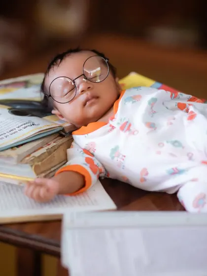 A close-up portrait of a sleeping newborn wearing oversized glasses, resting on a stack of books. It's these little details that make a shoot special.