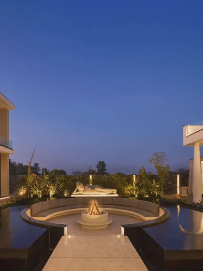 The Ananda courtyard at dusk, where the fire pit glows warmly and the architectural lighting creates a magical ambiance. This space embodies our commitment to creating homes that enhance wellness and provide a peaceful escape.